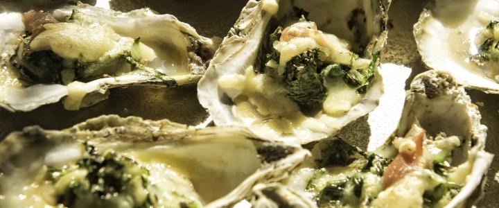 Close-up of baked oysters topped with melted cheese, herbs, and spinach on a tray.