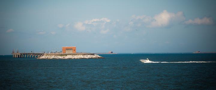 Speedboat on the water near a pier with a building, under a partly cloudy sky.