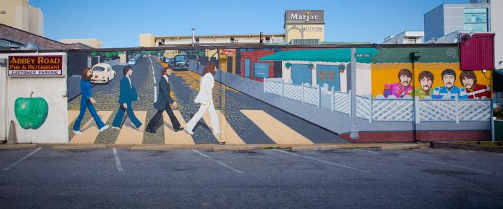 Mural depicting the Abbey Road album cover with The Beatles crossing a street, adjacent to a painted street scene featuring a cafe and the band's iconic Sgt. Pepper's outfits.
