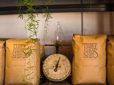 Bags labeled "Three Ships" on a shelf with a vintage scale and hanging plant.