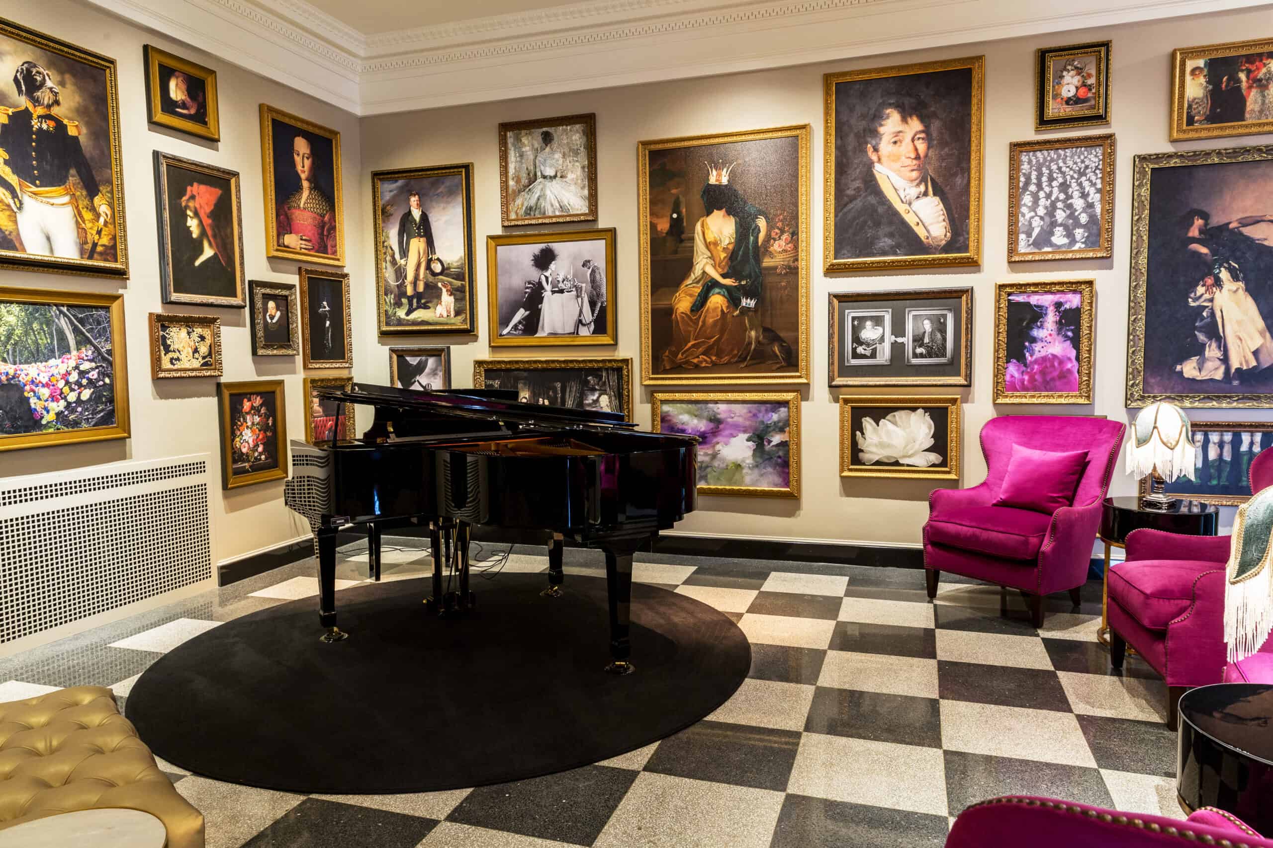 Room with a black grand piano surrounded by framed art on walls, featuring portraits and floral images. Pink armchairs and checkered flooring complete the decor.