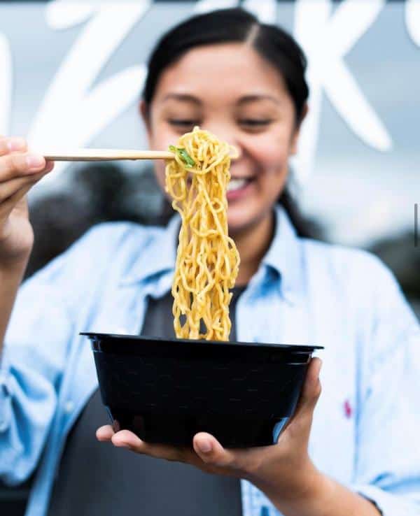 Person holding a bowl of noodles with chopsticks, smiling.