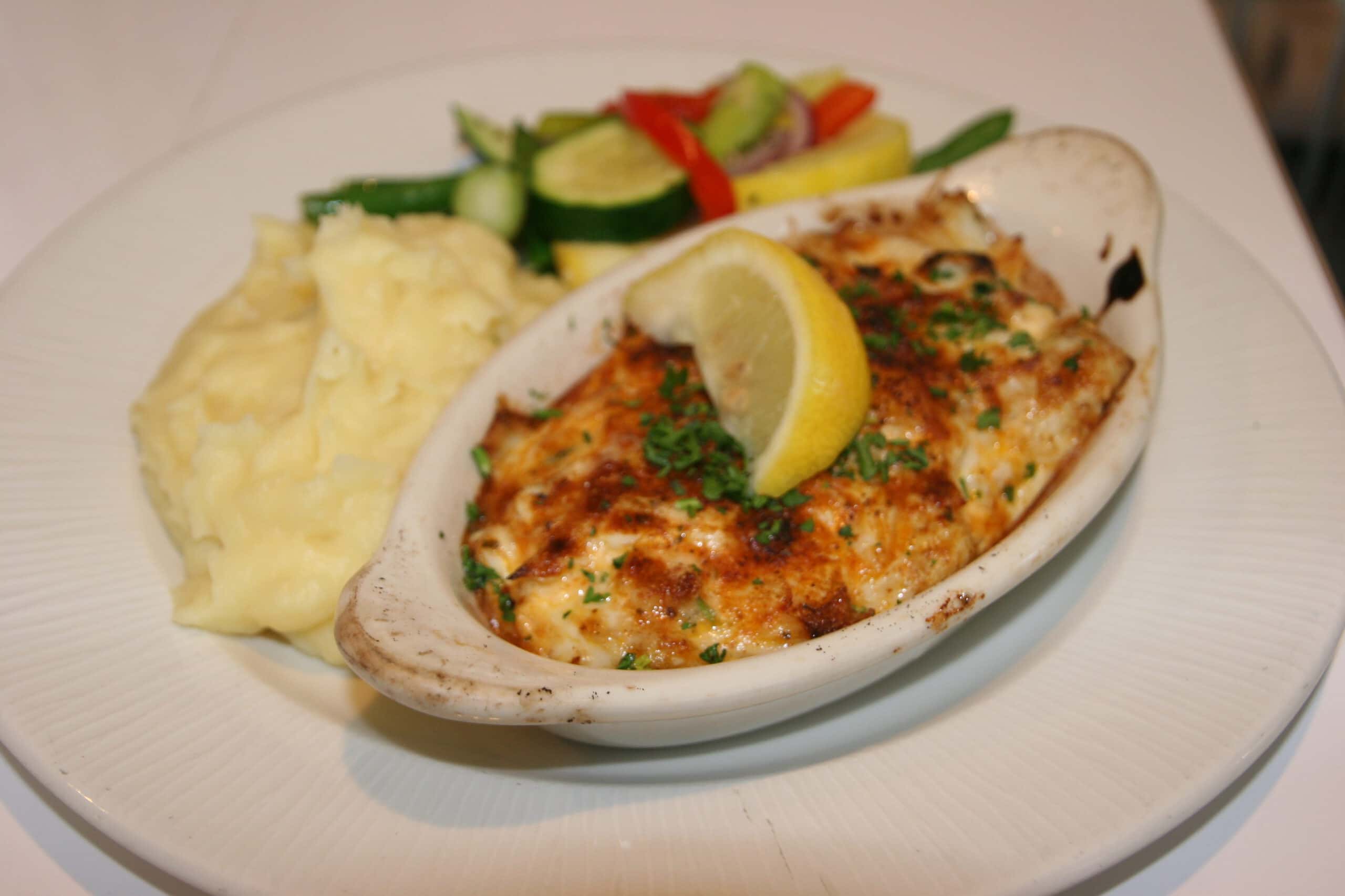Baked dish with a lemon wedge, mashed potatoes, and mixed vegetables on a white plate.