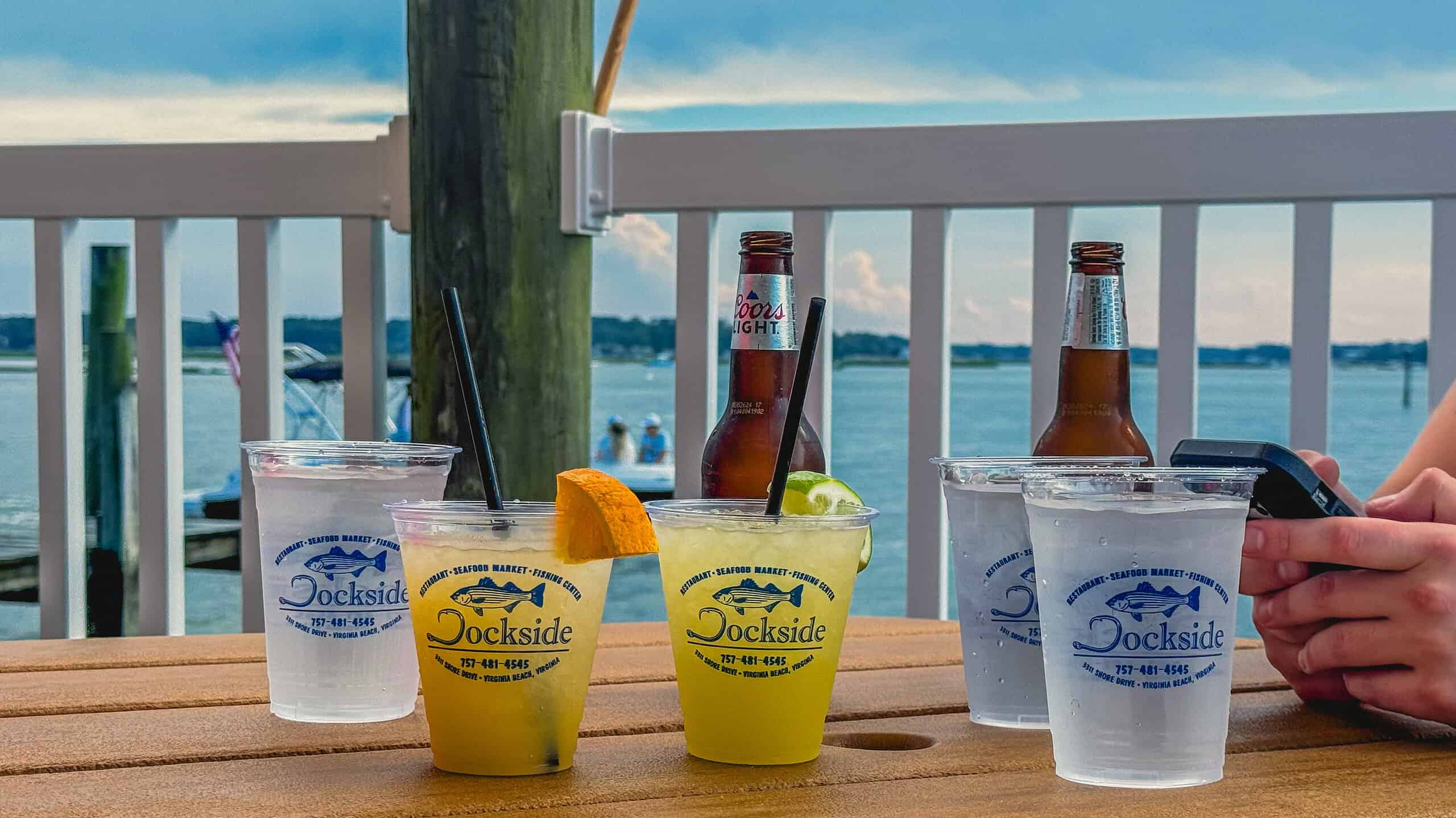 image of beer, water, and cocktail drinks on picnic table overlooking water and sunset on Lynnhaven Inlet