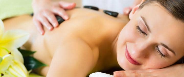 Person receiving a hot stone massage, lying face down with eyes closed.