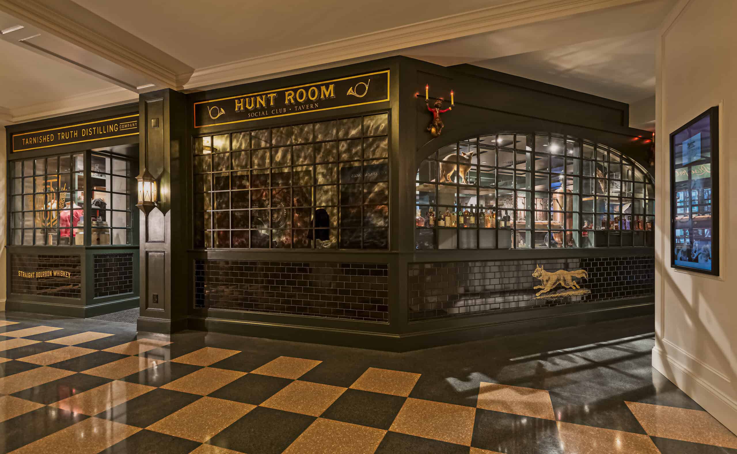 Dimly lit bar with glass panel windows, black and green decor, "Hunt Room" sign, and checkered floor tiles.