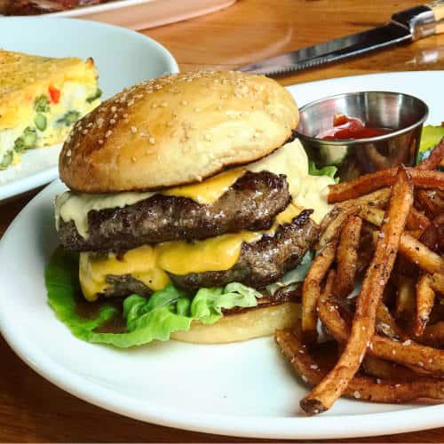 A double cheeseburger with lettuce on a plate next to crispy fries and a small cup of ketchup.