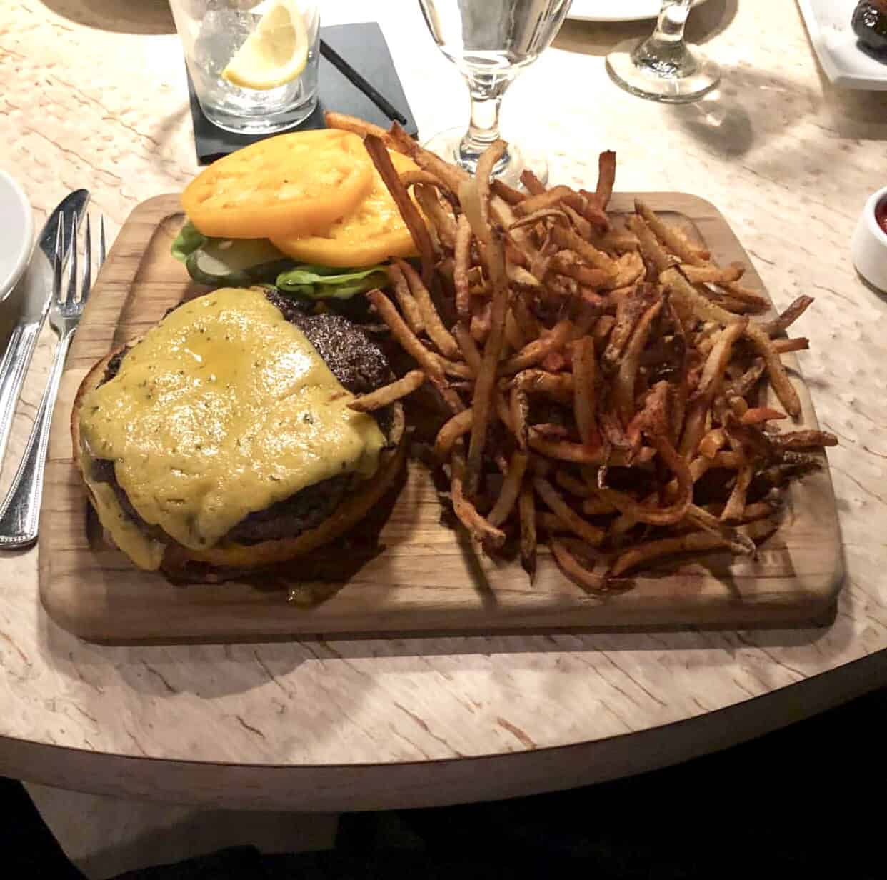 Cheeseburger with lettuce and tomato on a wooden board, served with a large portion of fries.