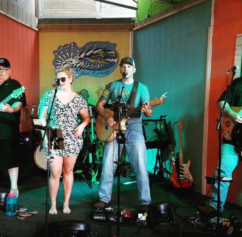 Band performing on a colorful indoor stage with a singer and guitarist in the foreground.