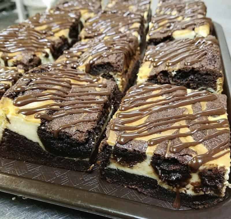 Several pieces of marbled cheesecake brownies drizzled with chocolate are arranged neatly on a tray.