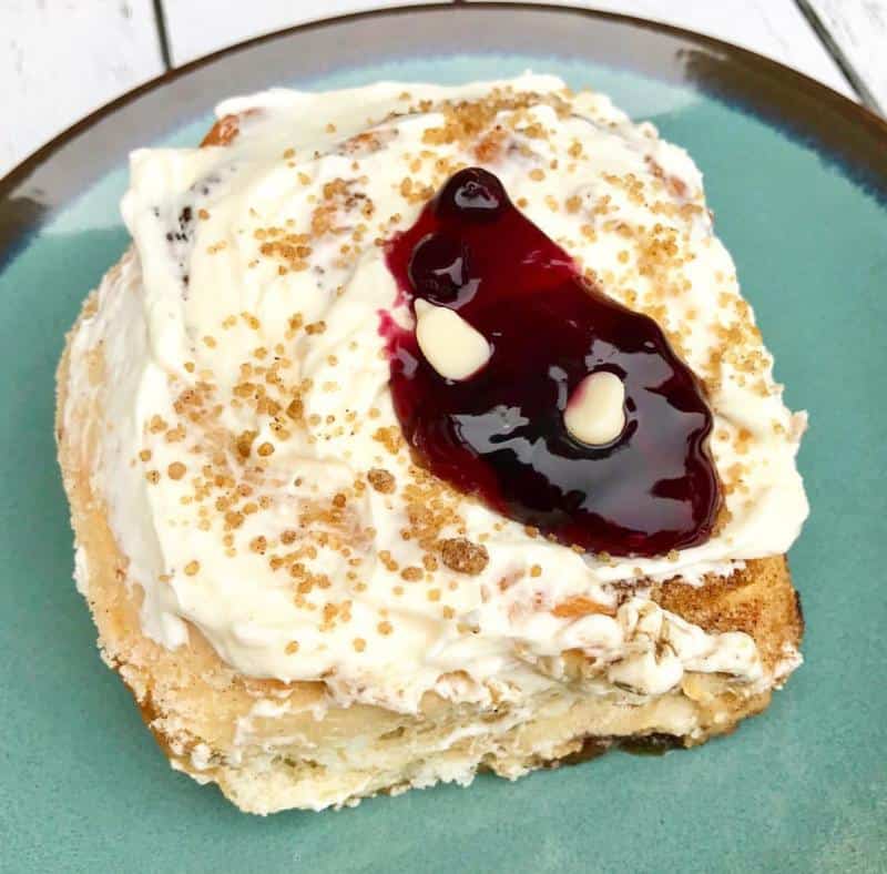 A pastry topped with white frosting, brown sugar, and a swirl of berry sauce sits on a green plate.