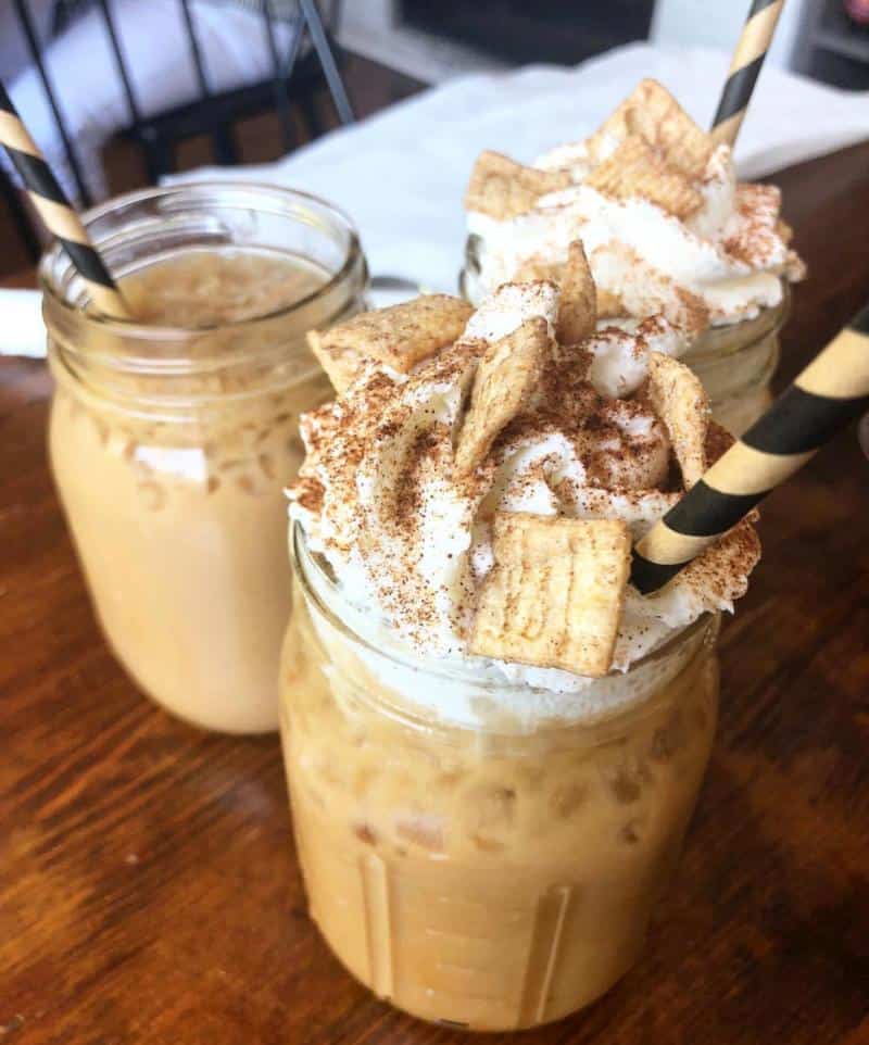 Three iced coffee drinks in mason jars, topped with whipped cream and cereal, with black and yellow striped straws.