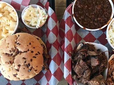 Plates with a burger, macaroni and cheese, coleslaw, baked beans, brisket, and pulled pork on checkered paper.