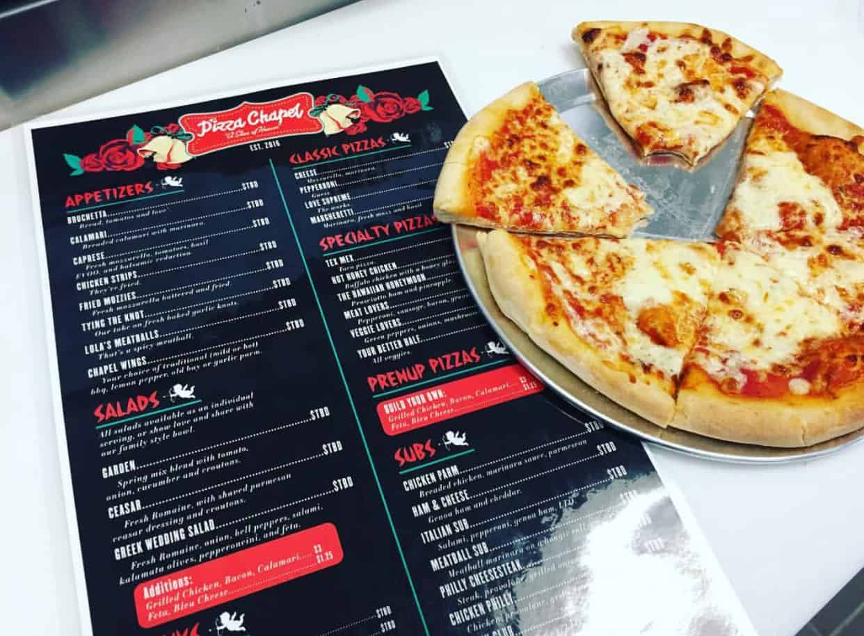 Menu and sliced cheese pizza on a metal tray, with one slice missing.