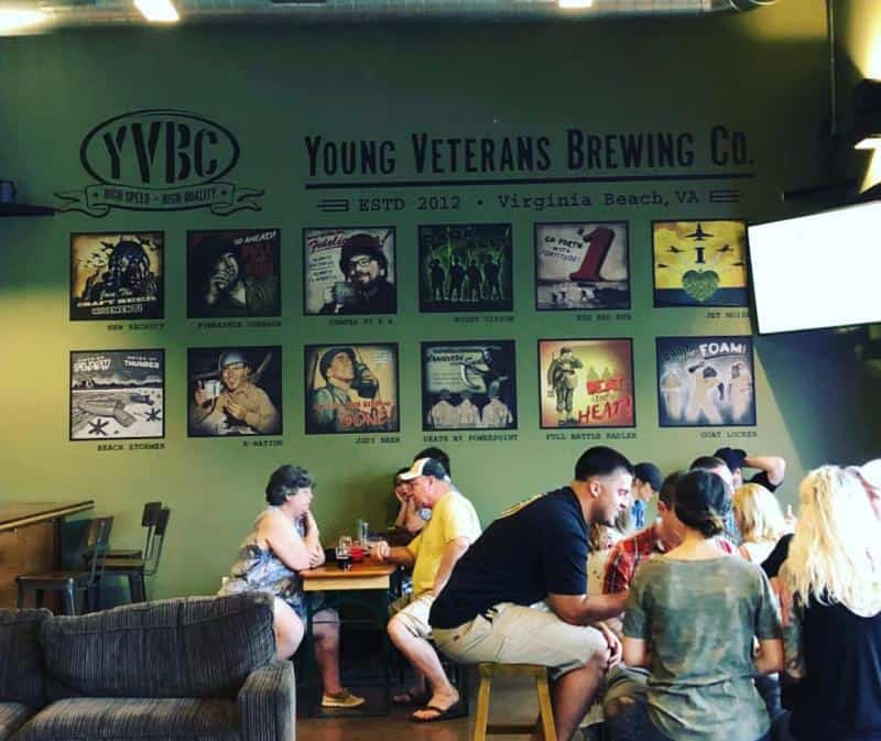 Group of people at Young Veterans Brewing Co. in Virginia Beach, sitting around tables under a wall with various posters.