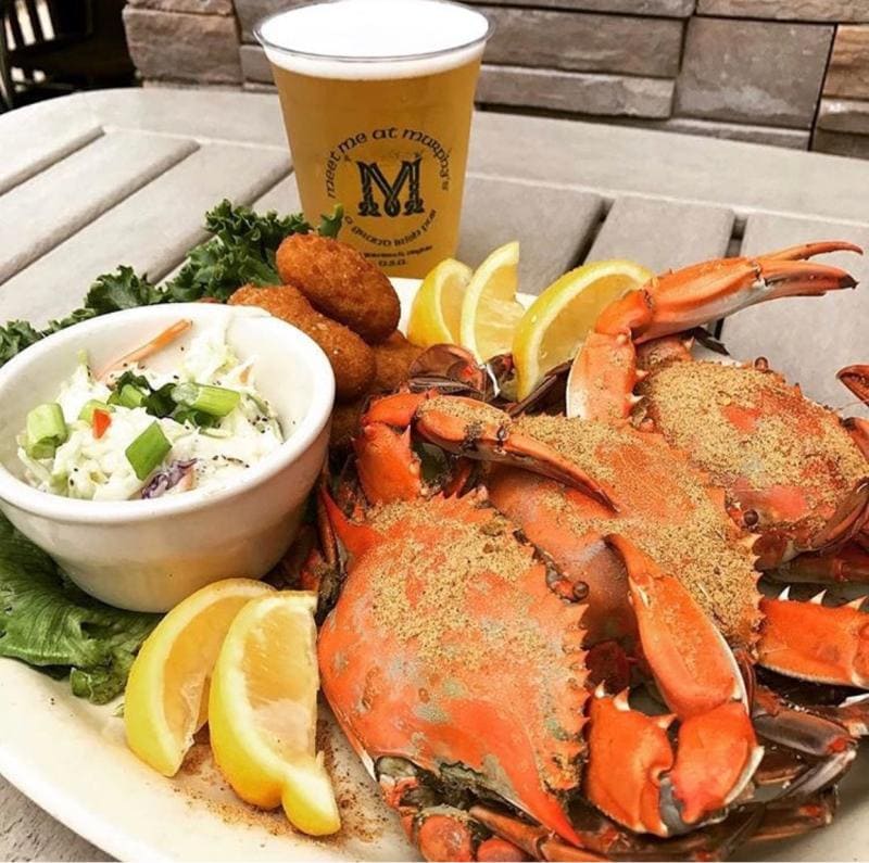Plate of steamed crabs with lemon wedges, coleslaw, and hush puppies, accompanied by a beer in a glass on a table.