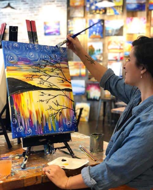 Person painting a colorful landscape on a canvas in an art studio.