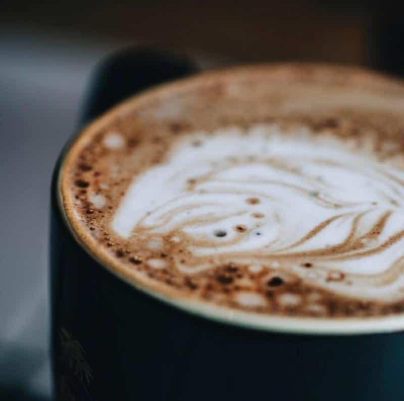 A close-up of a frothy cappuccino in a dark cup, showcasing latte art on the surface.