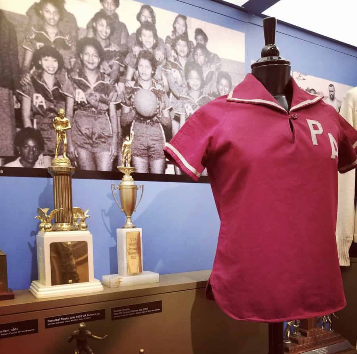 Display of a vintage sports jersey on a mannequin with several trophies and a historic team photo in the background.