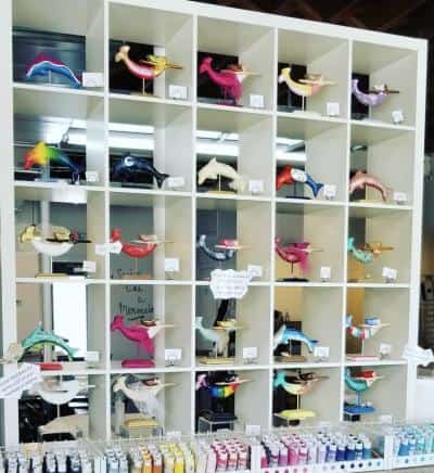 A display shelf with multiple compartments, each containing differently colored and shaped sculptures of birds. Below the compartments are rows of small paint tubes.