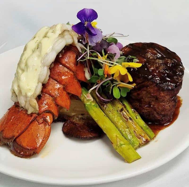 Steak and lobster tail with asparagus and decorative flowers on a white plate.