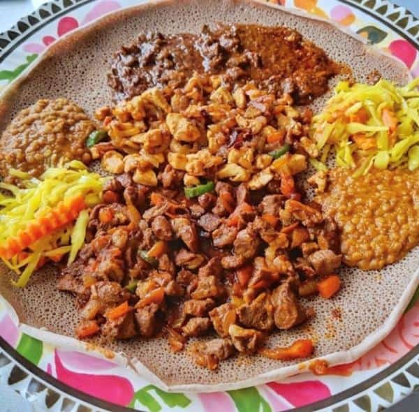 Plate of injera topped with various Ethiopian dishes, including stews and vegetables, displayed on a colorful platter.