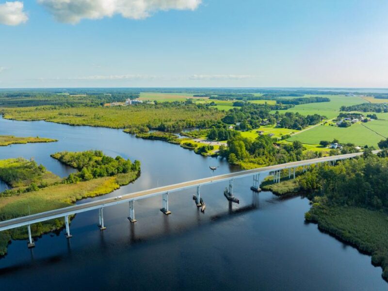 Aerial view of a bridge over a river surrounded by lush greenery and expansive farmland.