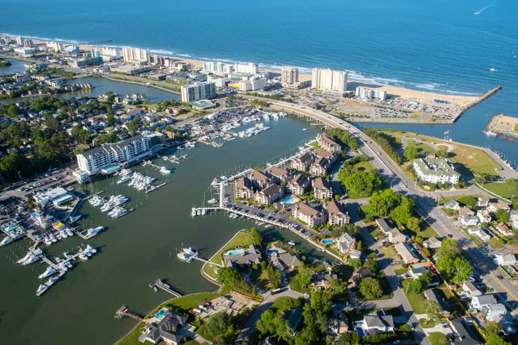 Aerial view of a coastal marina with boats, residential areas, and sandy beach along the ocean shoreline.