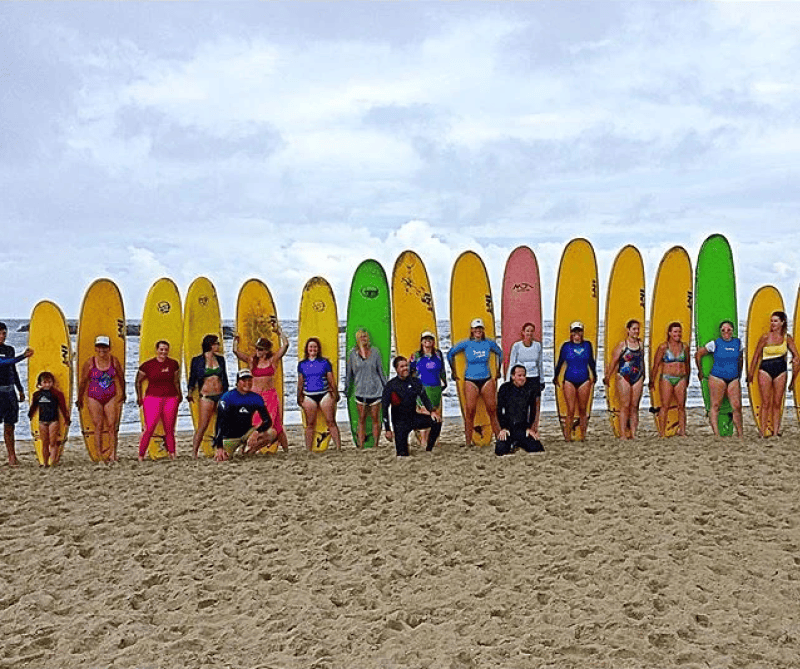 Group of people pose with colorful surfboards on a sandy beach under a cloudy sky.