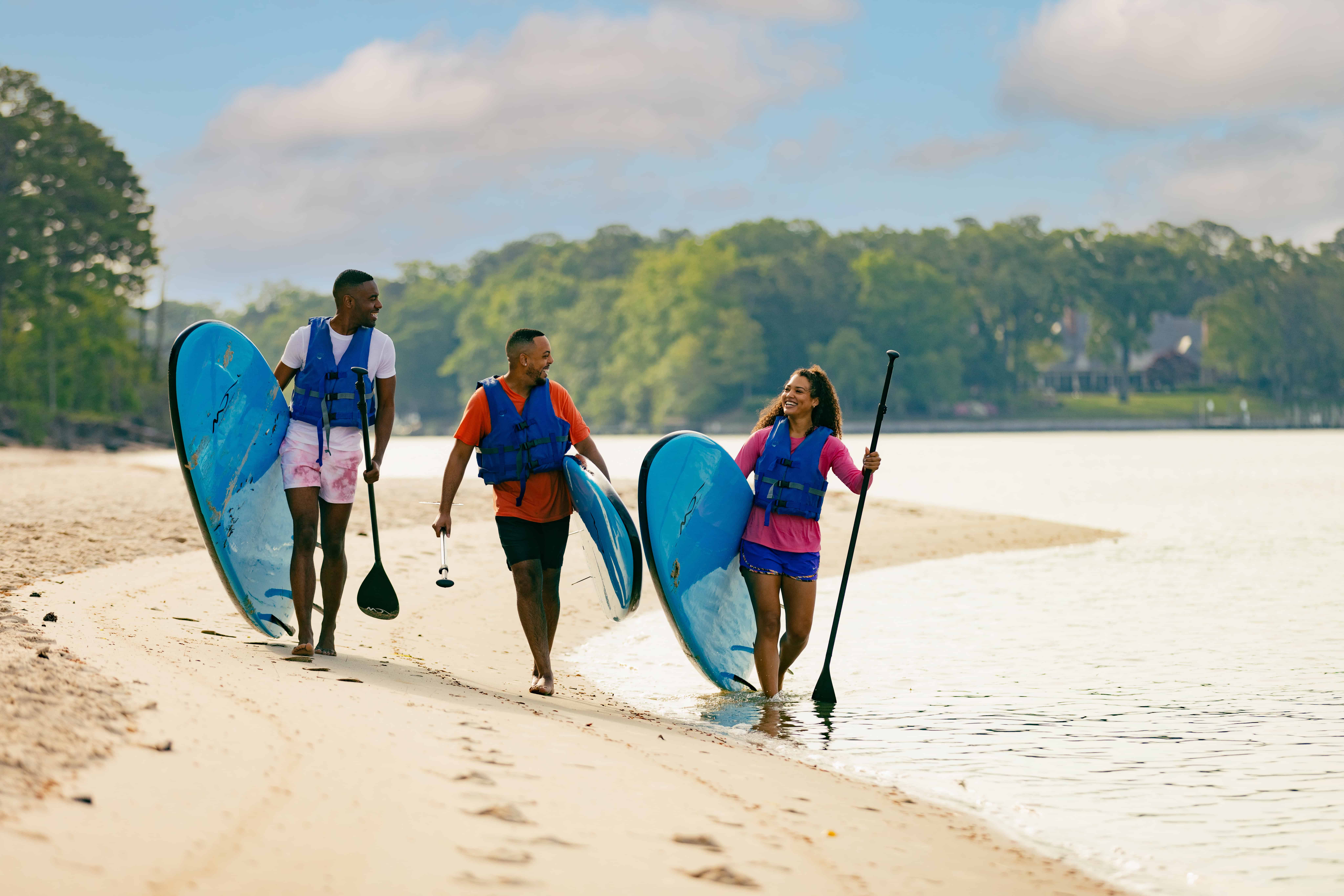 three people carrying SUP boards on the beach