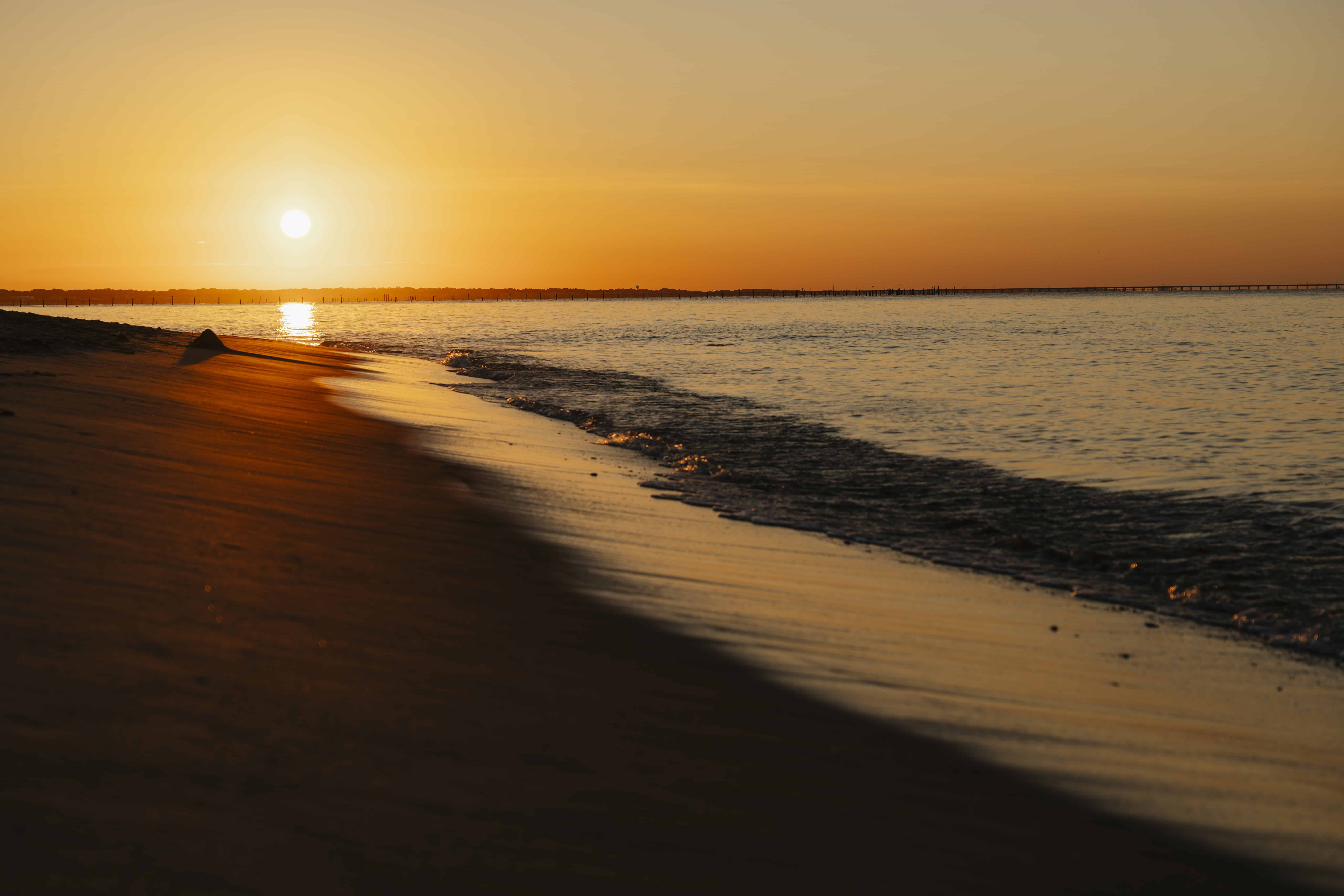 Sunset over a tranquil beach, with golden reflections on the water and a smooth shoreline.