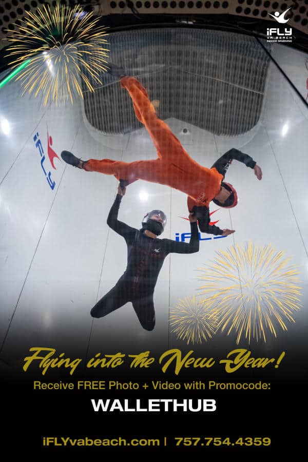 Two people in flight suits perform indoor skydiving. Fireworks graphics and promotional text overlay the image.