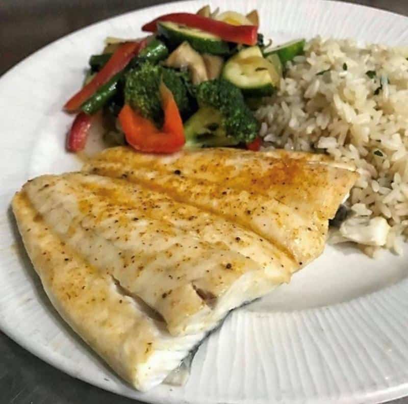 Grilled fish fillet with seasoned rice and mixed vegetables on a white plate.