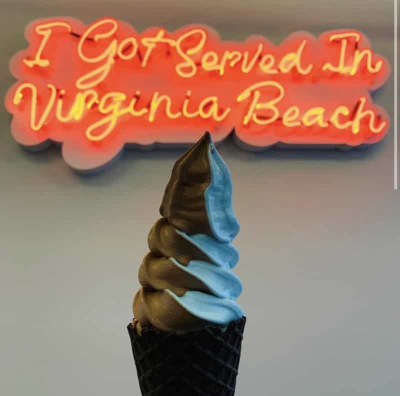 Soft serve ice cream in a black waffle cone, with a neon sign in the background reading, "I Got Served in Virginia Beach.