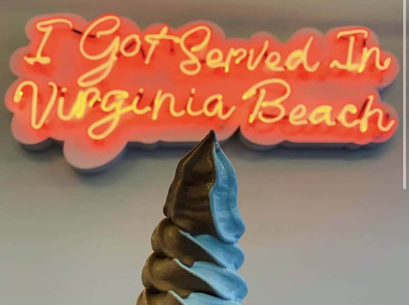 Two flavors swirled together in an Aqua S soft-serve waffle cone with a neon sign on the wall behind that reads, 