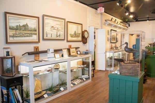 Museum exhibit room with glass display cases containing artifacts, paintings on the walls, a clock, and decorative items.