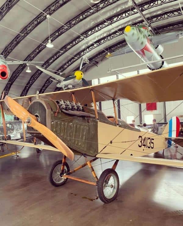 Vintage biplane with wooden propeller displayed in an aircraft hangar alongside other aircraft, featuring a military design and the number "34135" on its side.