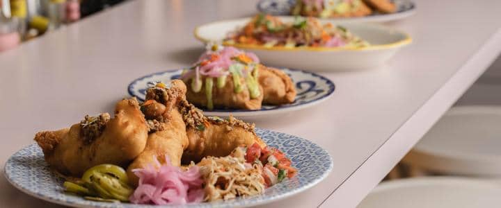 Close-up of three plates with fried food garnished with pickled onions and herbs, arranged in a line on a white counter.
