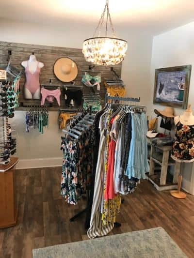 Boutique with racks of colorful clothing and swimwear, a chandelier overhead, and a decorative wall display.