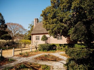 The historic Adam Thoroughgood House surrounded by lush gardens and well-maintained hedges under a clear blue sky.