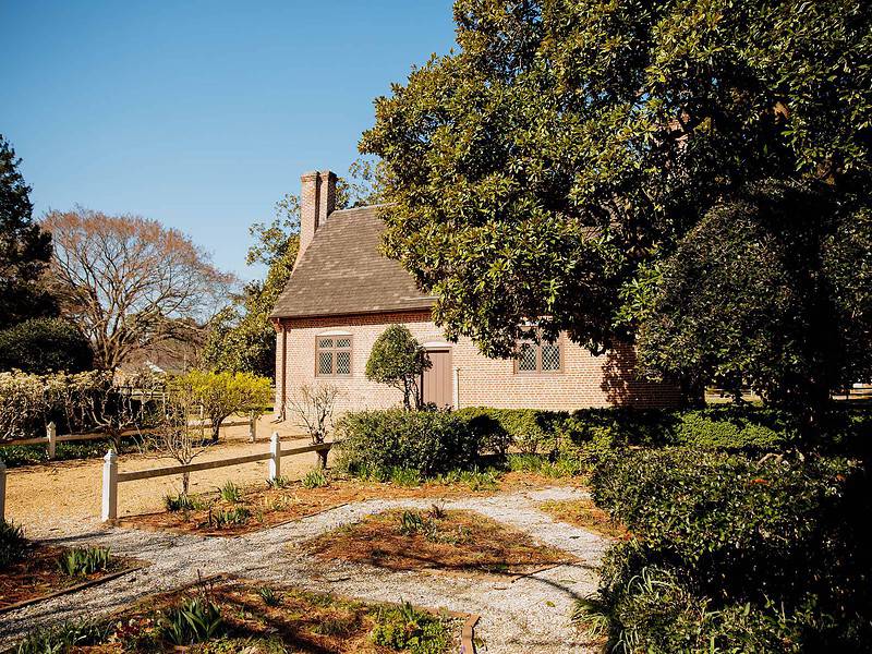 The historic Adam Thoroughgood House surrounded by lush gardens and well-maintained hedges under a clear blue sky.