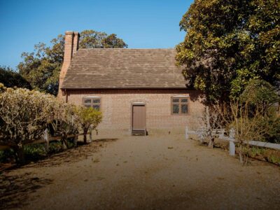 The historic Adam Thoroughgood House surrounded by lush gardens and well-maintained hedges under a clear blue sky.