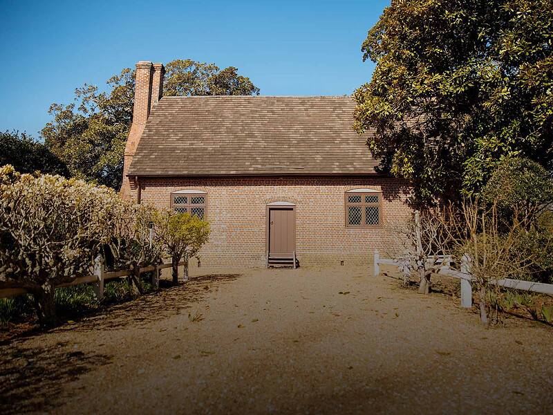 The historic Adam Thoroughgood House surrounded by lush gardens and well-maintained hedges under a clear blue sky.