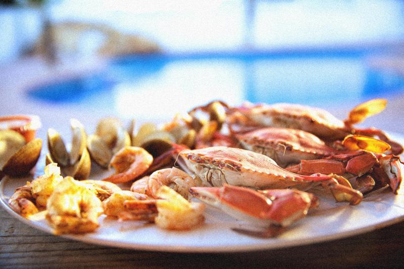 A plate of mixed seafood with crabs, shrimp, and clams on a wooden table by a poolside.