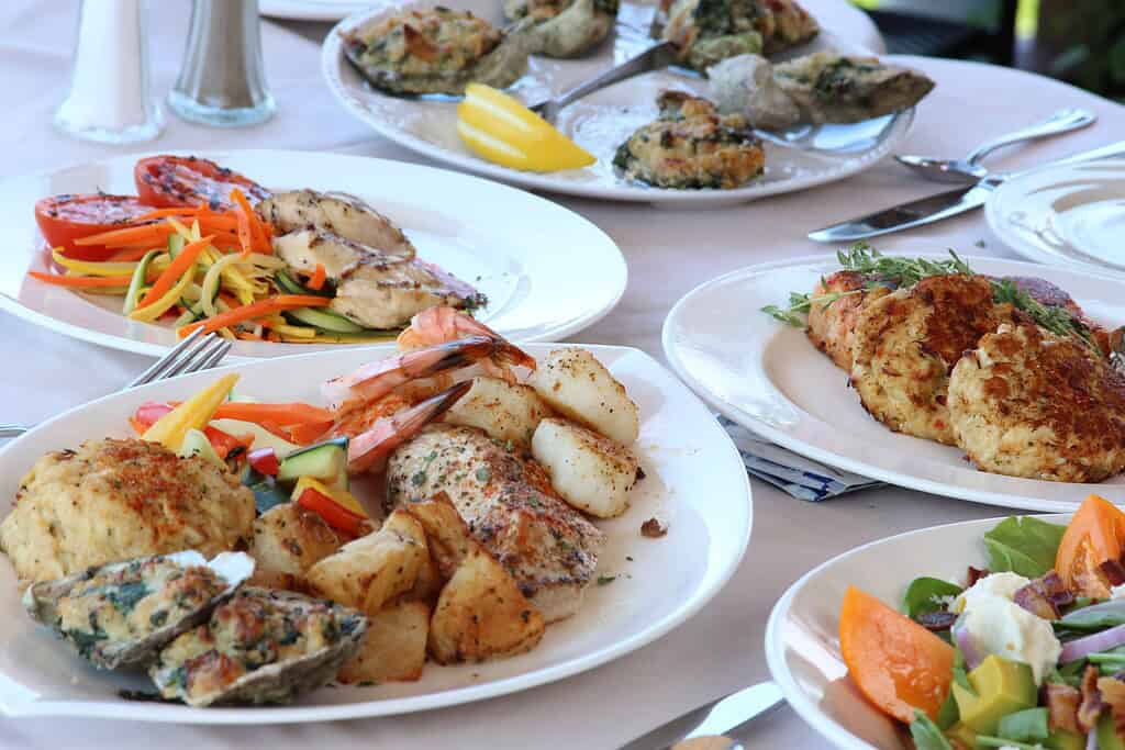 A vibrant seafood platter featuring grilled chicken, shrimp, scallops, stuffed oysters, and colorful vegetable sides.