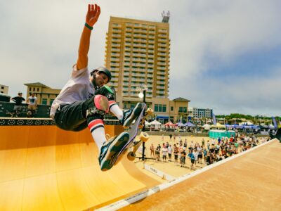 Skateboarder performing an aerial trick on a ramp at the Jackalope Festival, with a crowd watching and buildings in the background.