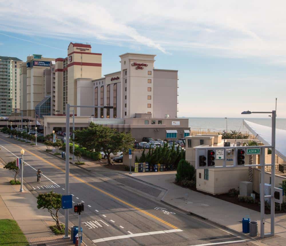 View of a coastal street featuring the Hampton Inn and nearby hotels, with a cyclist and traffic signals, along the beach.