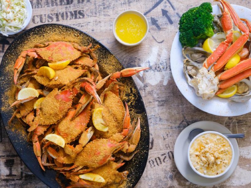 A platter of seasoned crabs with lemon slices, accompanied by a side of broccoli, coleslaw, and a bowl of crab chowder.