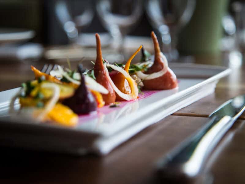 A gourmet dish featuring colorful vegetables arranged artistically on a white plate, garnished with herbs and a vibrant sauce.