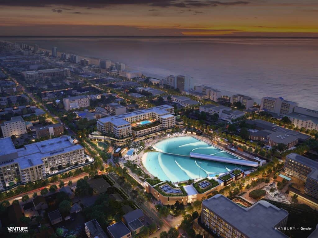 Aerial view of a coastal development featuring modern buildings, a large lagoon, and lush landscaping at sunset.